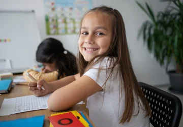 Menina sorrindo em sala de aula durante atividade sobre o Dia Mundial da Língua Portuguesa.
