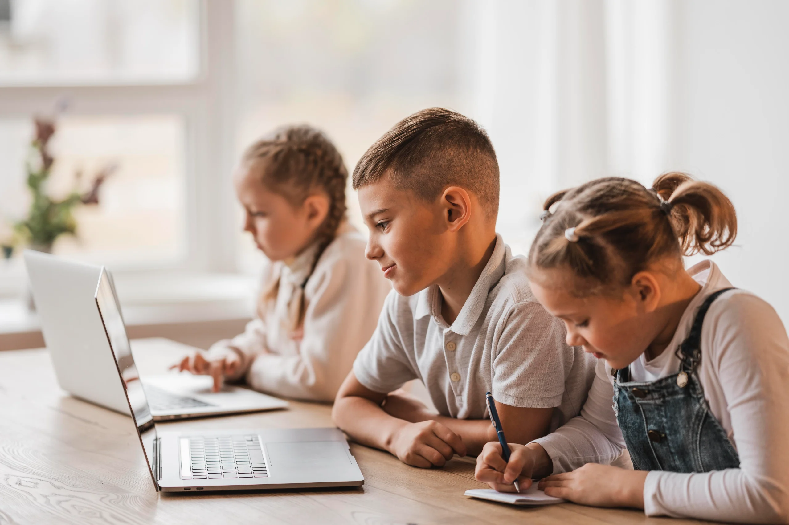Estudantes em sala de aula usando laptops e caderno em escola que usa Geekie One.