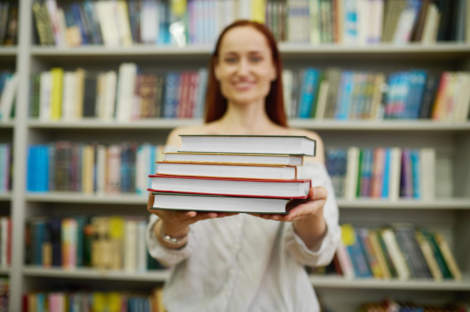 Professora mostra pilha de livros de material didático para o ensino fundamental em biblioteca escolar.