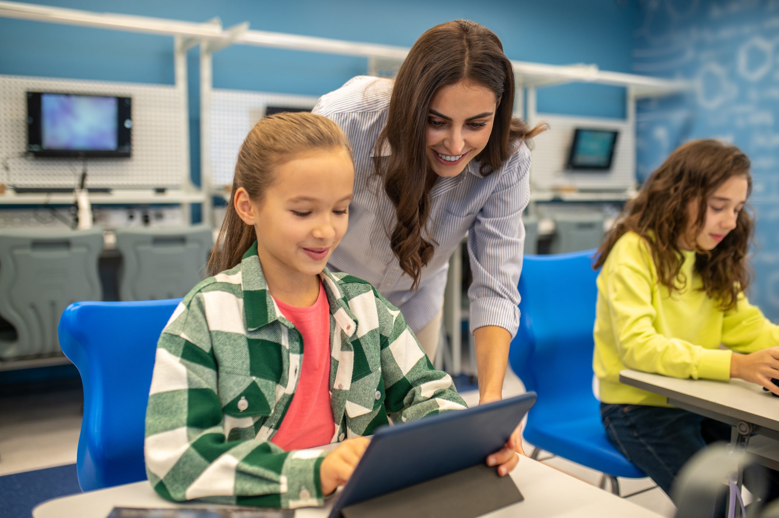 Professora orientando aluna no uso de tablet durante atividade de formação docente com tecnologia educacional.